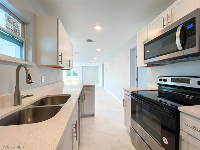 kitchen with stainless steel appliances, light tile floors, sink, white cabinets, and light stone counters