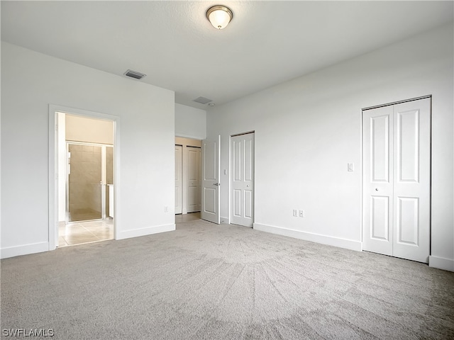 unfurnished bedroom featuring light carpet, connected bathroom, and two closets