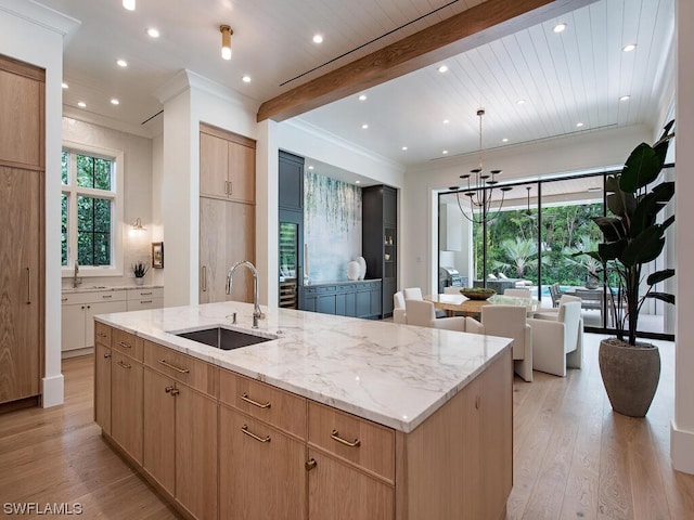 kitchen featuring light stone countertops, light hardwood / wood-style flooring, sink, and a kitchen island with sink