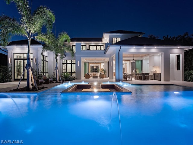 back house at night featuring a patio area and pool water feature