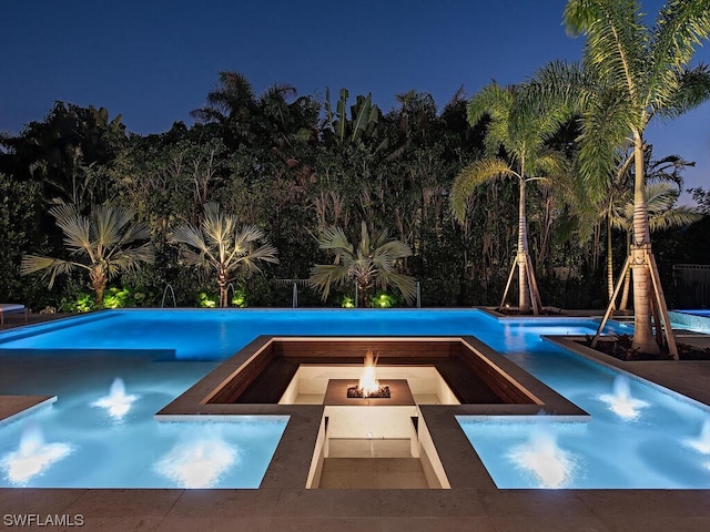 pool at night with an outdoor fire pit and a patio