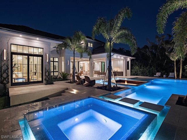 pool at night with a patio area and an in ground hot tub