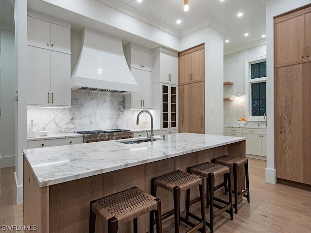 kitchen with white cabinetry, custom range hood, backsplash, and sink