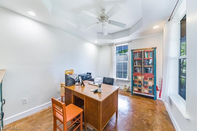 office area with concrete floors, ceiling fan, and a tray ceiling