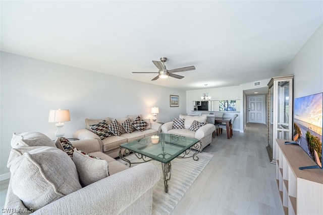 living room featuring ceiling fan with notable chandelier and light wood-type flooring