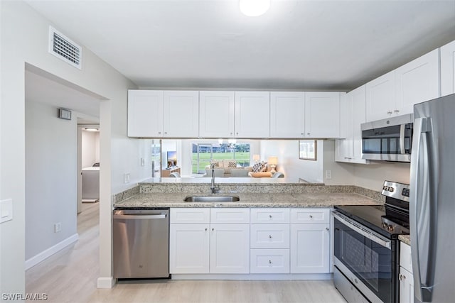 kitchen with light hardwood / wood-style floors, stainless steel appliances, white cabinetry, sink, and light stone counters