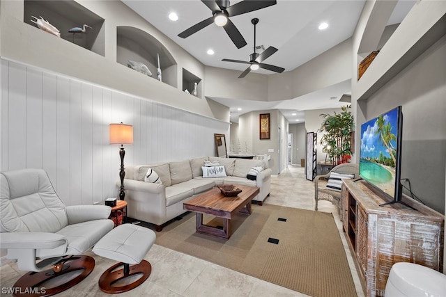 tiled living room with wood walls, ceiling fan, and a towering ceiling