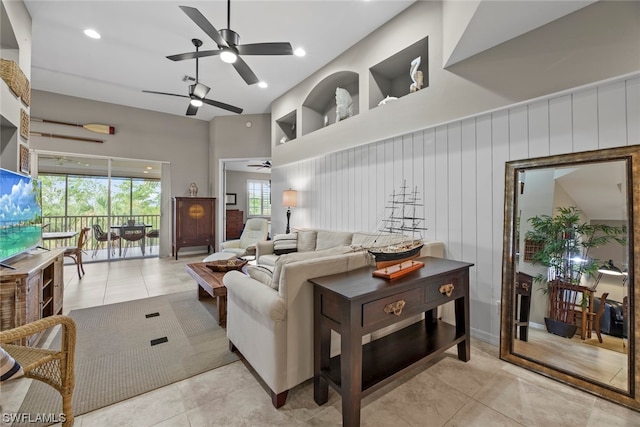 living room featuring a high ceiling, ceiling fan, wooden walls, and light tile patterned floors