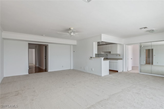 unfurnished living room with light colored carpet, crown molding, a ceiling fan, and visible vents