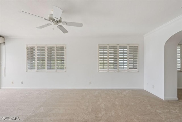 carpeted spare room with baseboards, arched walkways, a ceiling fan, and crown molding