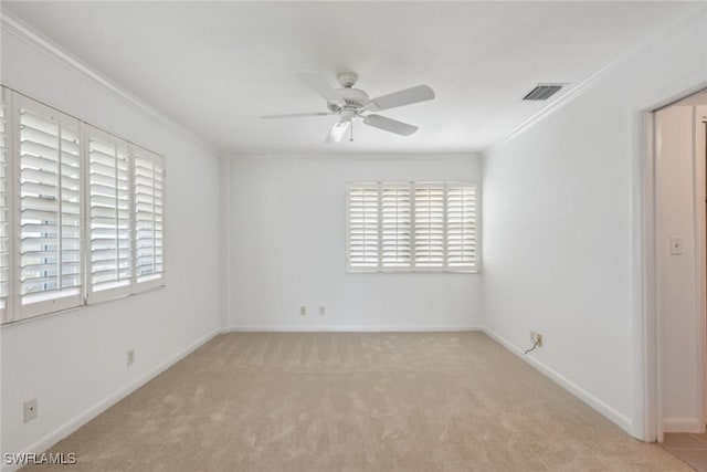 carpeted spare room with visible vents, baseboards, ceiling fan, and crown molding