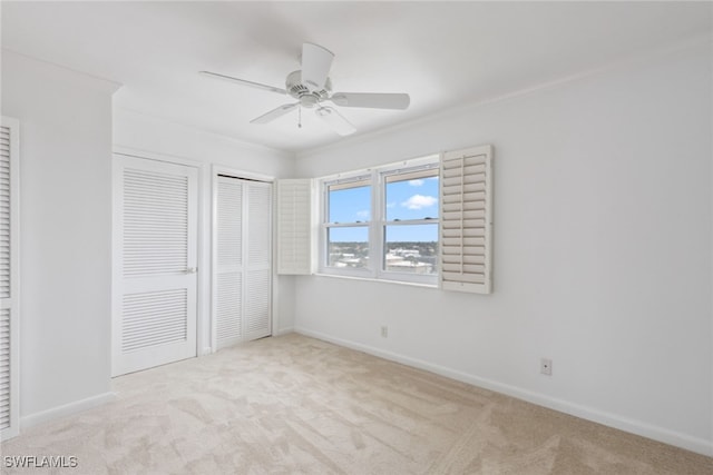 unfurnished bedroom with two closets, ceiling fan, light colored carpet, and ornamental molding