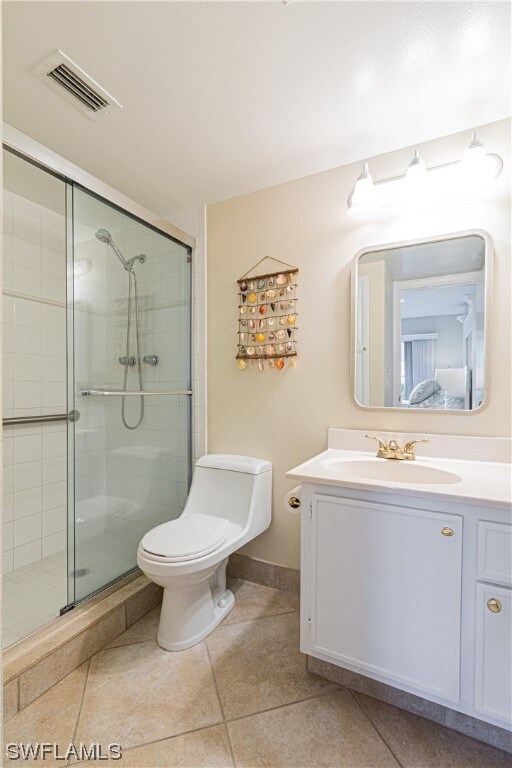 bathroom featuring oversized vanity, toilet, a shower with shower door, and tile flooring