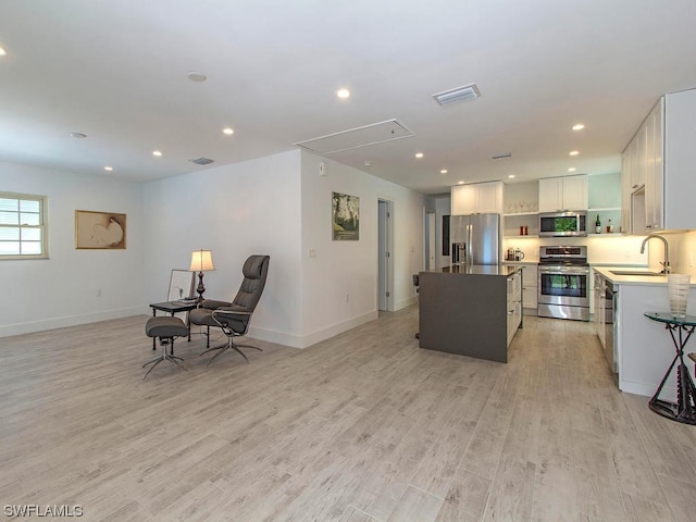 kitchen with sink, stainless steel appliances, a center island, light hardwood / wood-style floors, and white cabinets