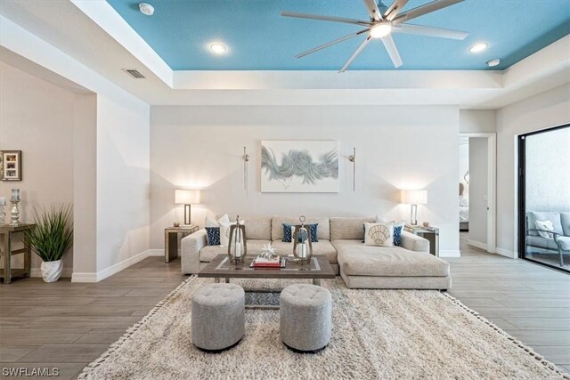 living room featuring ceiling fan, hardwood / wood-style floors, and a tray ceiling