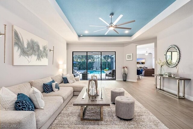 living room featuring light hardwood / wood-style flooring, ceiling fan, and a raised ceiling