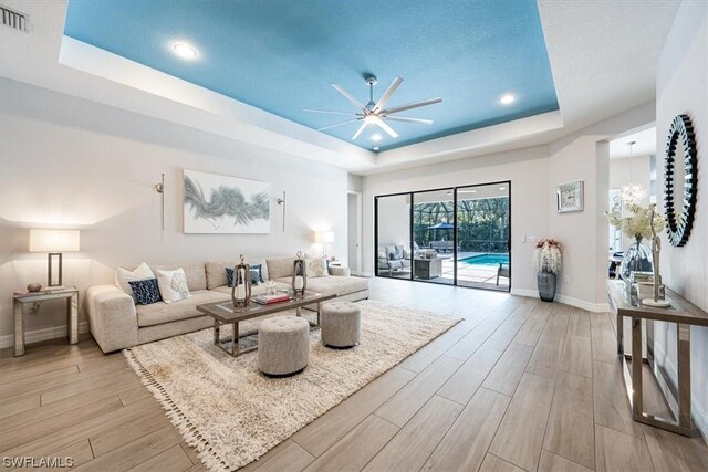 living room featuring a textured ceiling, light hardwood / wood-style flooring, ceiling fan, and a tray ceiling