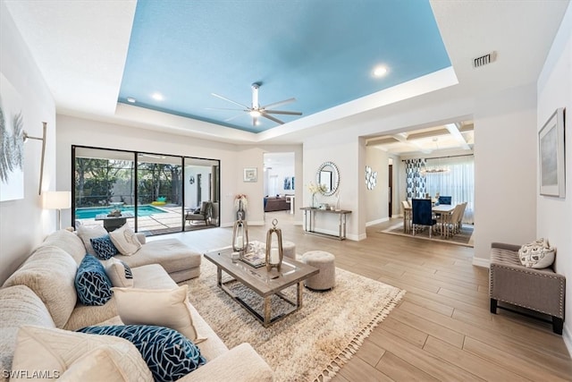 living room featuring a raised ceiling, ceiling fan, and light hardwood / wood-style floors