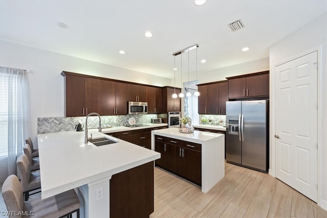 kitchen with hanging light fixtures, appliances with stainless steel finishes, sink, a kitchen bar, and dark brown cabinetry