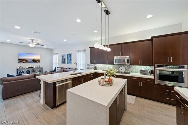 kitchen with light wood-type flooring, decorative light fixtures, stainless steel appliances, sink, and ceiling fan