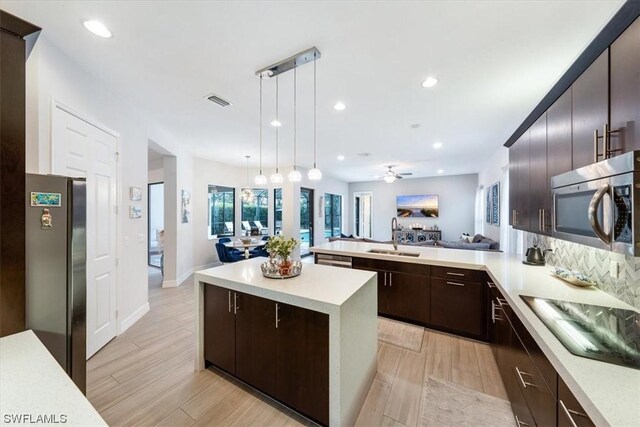 kitchen with hanging light fixtures, appliances with stainless steel finishes, light hardwood / wood-style floors, sink, and a kitchen island