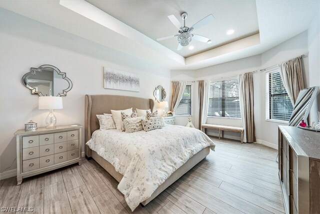 bedroom with light wood-type flooring, a raised ceiling, and ceiling fan