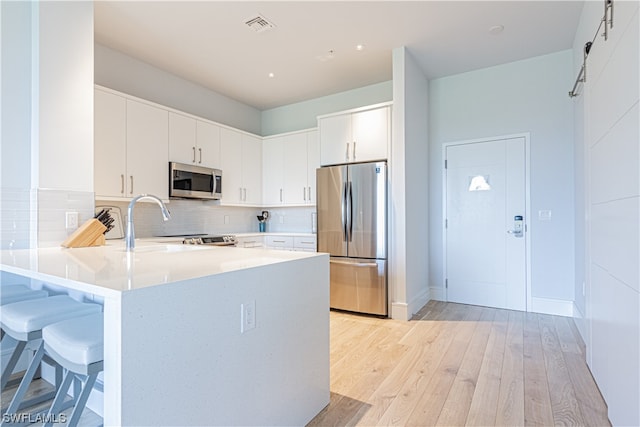 kitchen featuring a barn door, white cabinets, appliances with stainless steel finishes, and light wood-type flooring