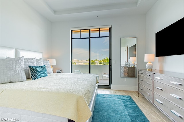 bedroom with access to exterior, a raised ceiling, and light hardwood / wood-style flooring