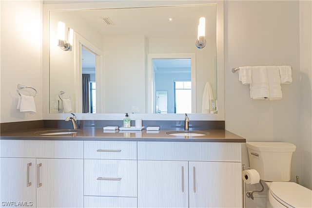 bathroom with toilet and dual bowl vanity