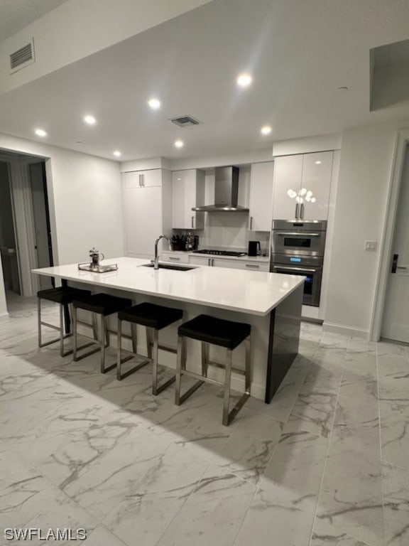 kitchen with wall chimney range hood, sink, light tile flooring, and white cabinetry