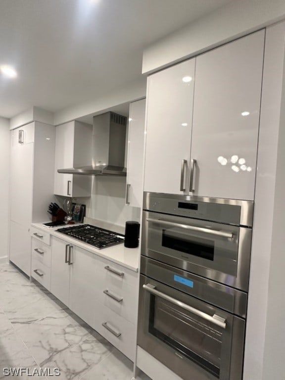 kitchen with wall chimney range hood, light tile flooring, white cabinetry, black gas stovetop, and stainless steel double oven