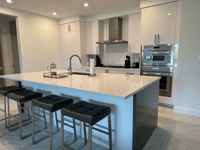 kitchen with wall chimney range hood, a kitchen breakfast bar, sink, and a center island with sink