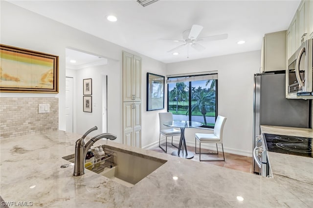 kitchen featuring light stone countertops, stainless steel appliances, ceiling fan, and sink