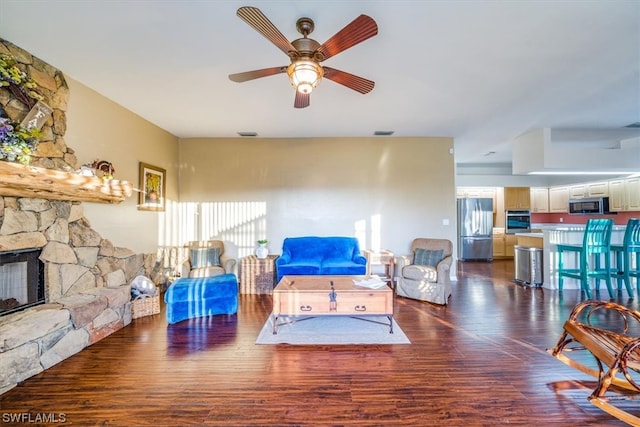 living room featuring dark hardwood / wood-style floors, ceiling fan, and a stone fireplace