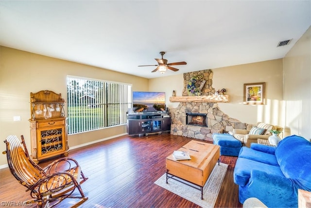 living room featuring dark wood-type flooring, a stone fireplace, and ceiling fan