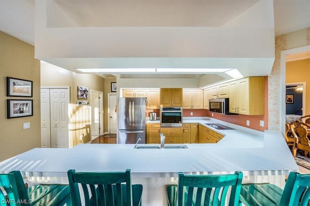 kitchen with kitchen peninsula, appliances with stainless steel finishes, a breakfast bar, sink, and light brown cabinetry