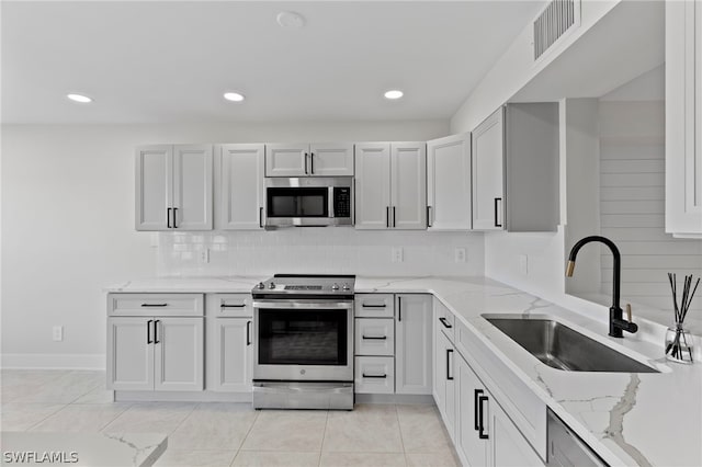 kitchen featuring appliances with stainless steel finishes, light stone counters, light tile patterned floors, and sink