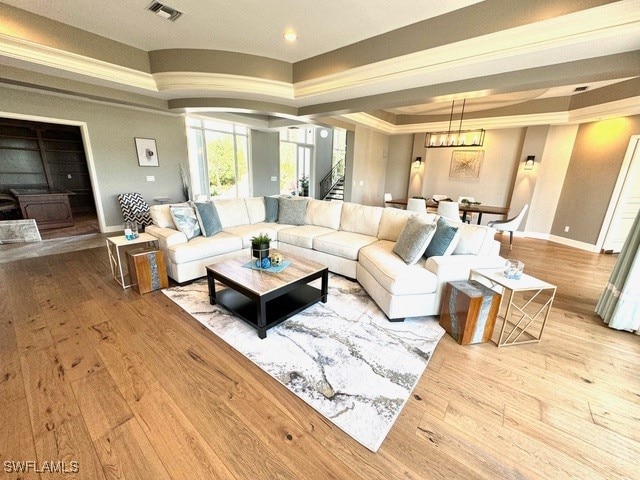 living room with an inviting chandelier, a tray ceiling, light hardwood / wood-style floors, and ornamental molding