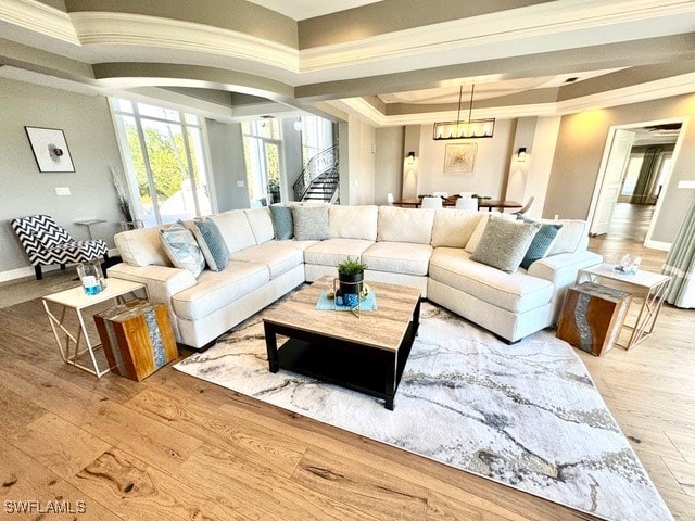 living room featuring crown molding, a raised ceiling, light hardwood / wood-style floors, and a notable chandelier