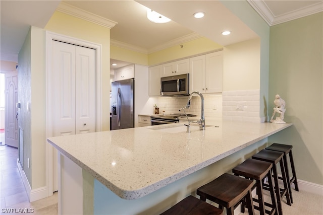 kitchen with kitchen peninsula, light stone counters, a kitchen breakfast bar, stainless steel appliances, and white cabinetry