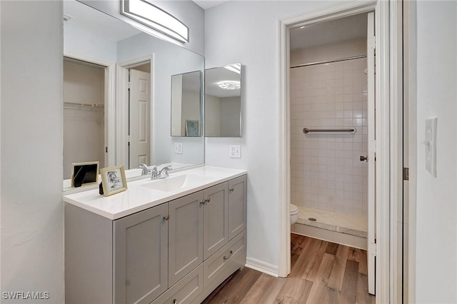 bathroom with vanity, toilet, a tile shower, and wood-type flooring