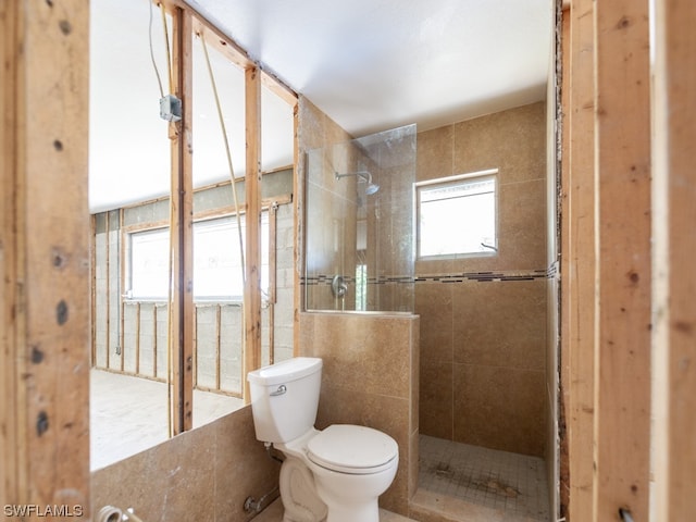 bathroom with tile walls, toilet, a tile shower, and a wealth of natural light