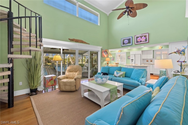 living room with a towering ceiling, ceiling fan, and light wood-type flooring