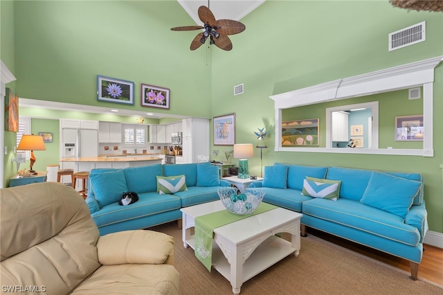 living room featuring a high ceiling, ceiling fan, and light wood-type flooring