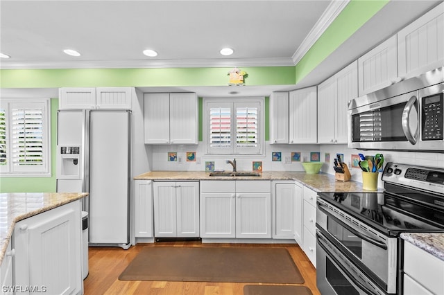 kitchen with white cabinets, appliances with stainless steel finishes, ornamental molding, and light wood-type flooring