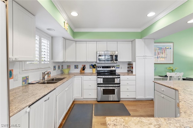 kitchen featuring appliances with stainless steel finishes, white cabinetry, light hardwood / wood-style flooring, and ornamental molding