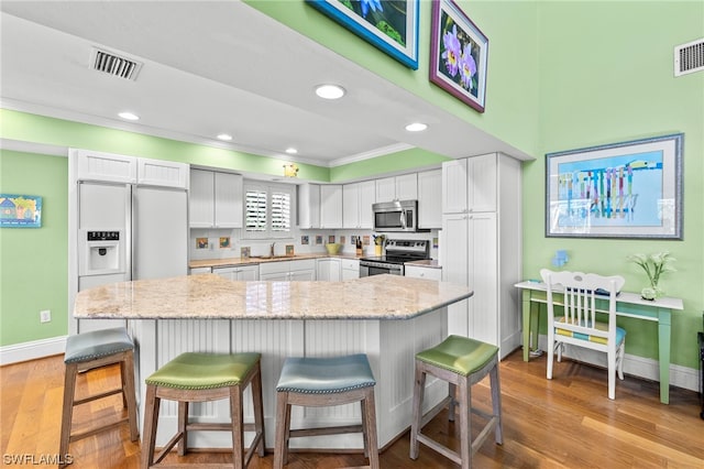 kitchen with a kitchen breakfast bar, appliances with stainless steel finishes, white cabinetry, and light wood-type flooring