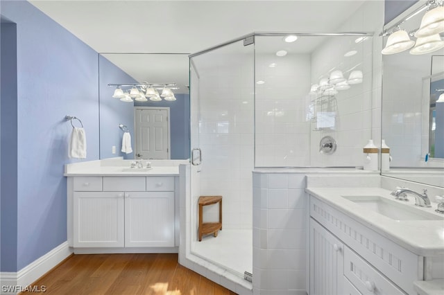 bathroom with a shower with door, vanity with extensive cabinet space, hardwood / wood-style floors, and double sink