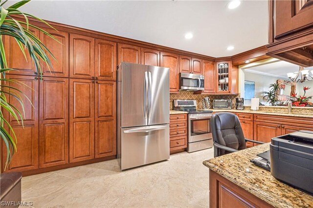 kitchen featuring sink, stainless steel appliances, tasteful backsplash, light stone counters, and a notable chandelier