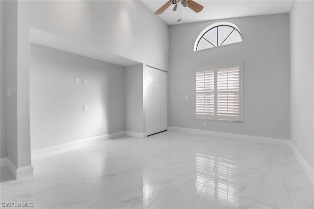 tiled spare room with ceiling fan and a high ceiling